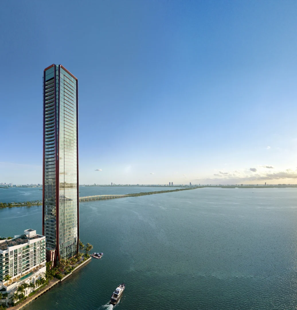 A tall skyscraper at Villa Miami stands beside blue water with a distant bridge and a boat below