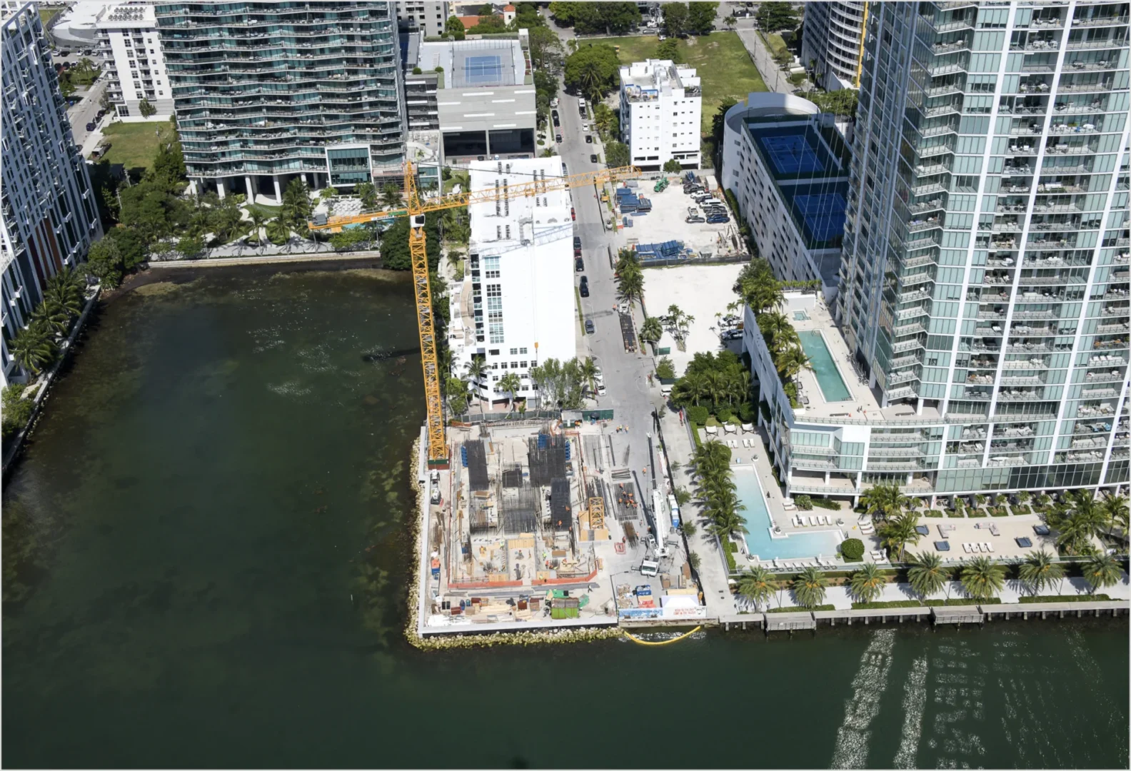 A yellow construction crane stands over a waterfront building site near high-rise buildings in Villa Miami