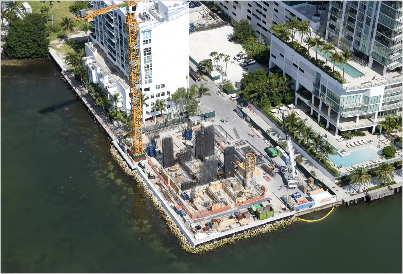 A large yellow crane stands over the Villa Miami construction site near water and white buildings