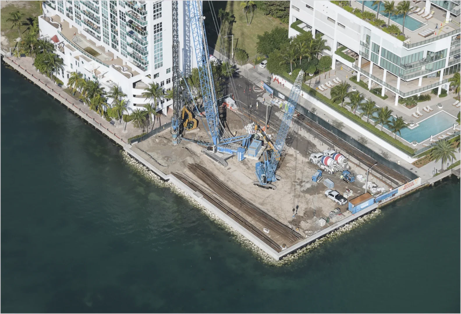 Large blue cranes and construction equipment sit on a waterfront site for Villa Miami next to high-rise buildings