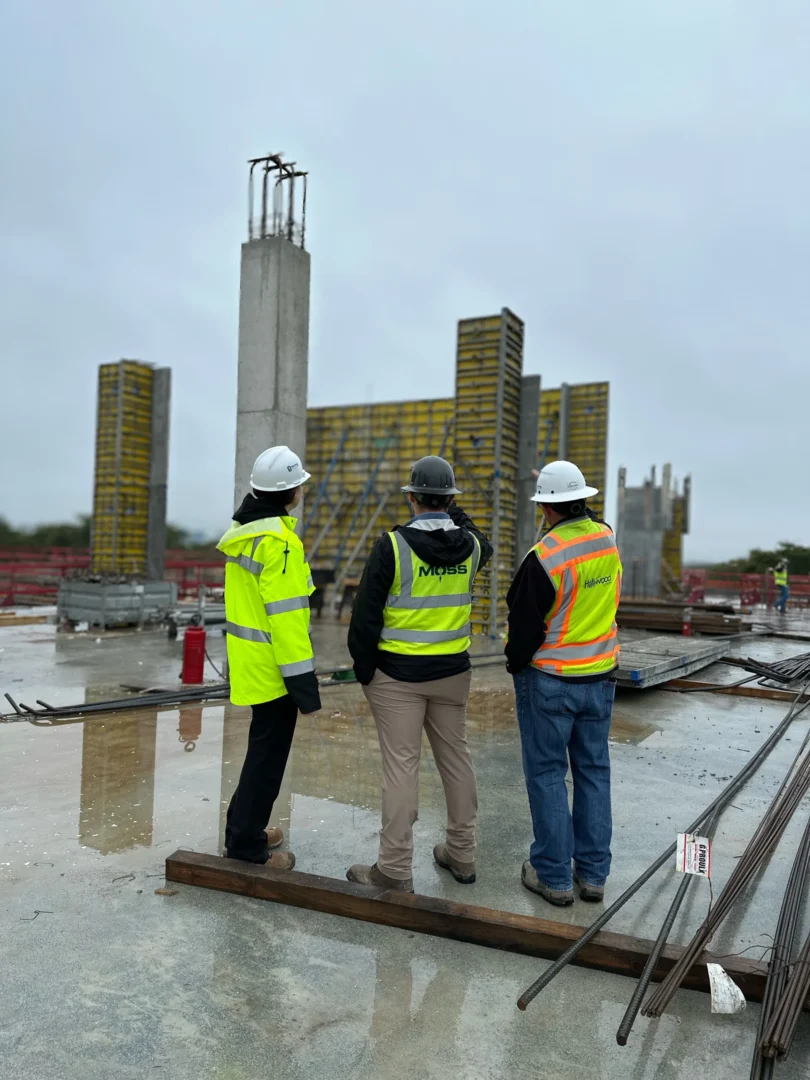 Three people in high-visibility vests and hard hats stand near concrete columns at the Hollywood Police Headquarters site