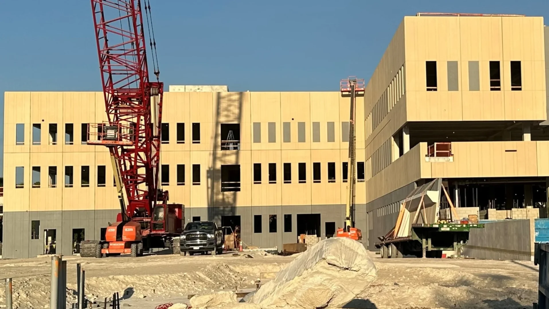 A large red lattice crane stands beside a tan building under construction at Hollywood Police Headquarters