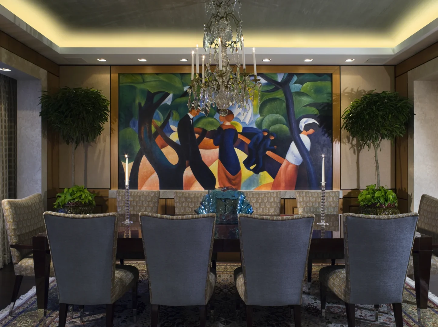 An abstract painting hangs behind a dining table and chairs under a crystal chandelier in the Penthouse 4 dining room