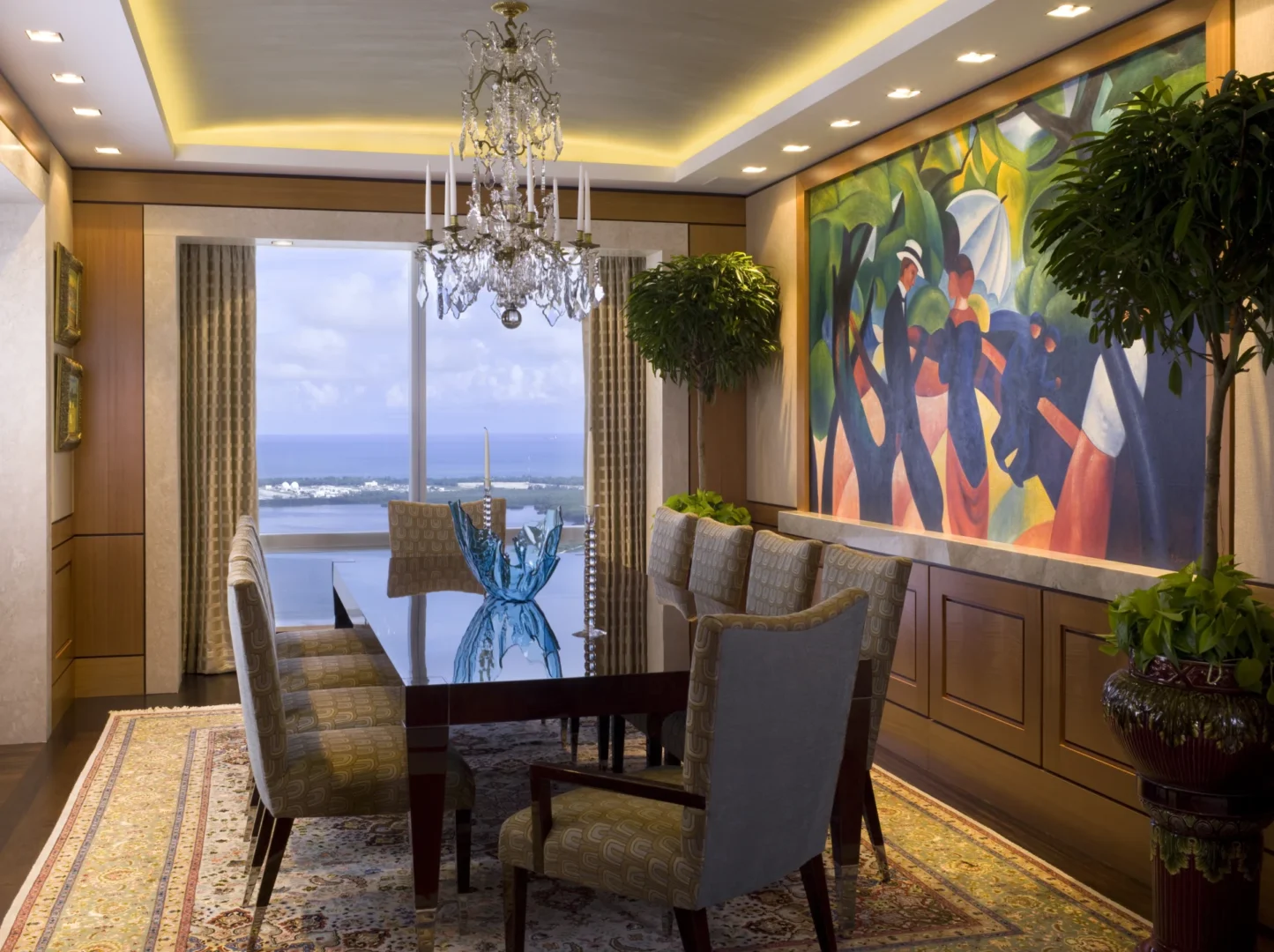A large abstract painting hangs in the Penthouse 4 dining room with a dining table, upholstered chairs, and a view of water