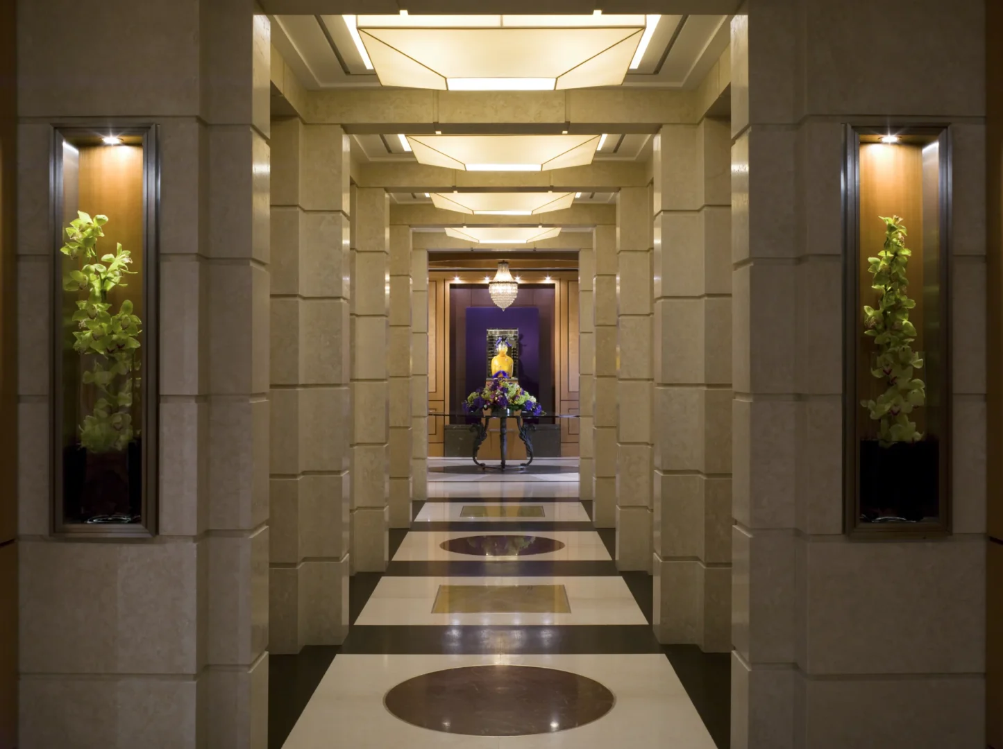 Symmetrical stone pillars line an illuminated corridor in Penthouse 4 that leads to a floral arrangement