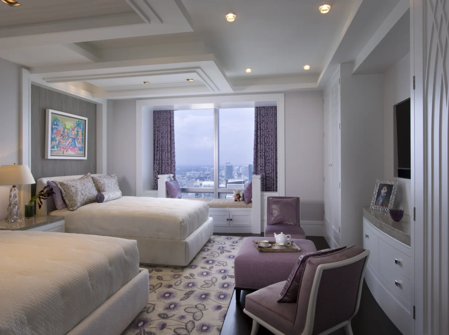 Two beds are located in the Penthouse 4 bedroom next to a large window with views of a city skyline and purple curtains