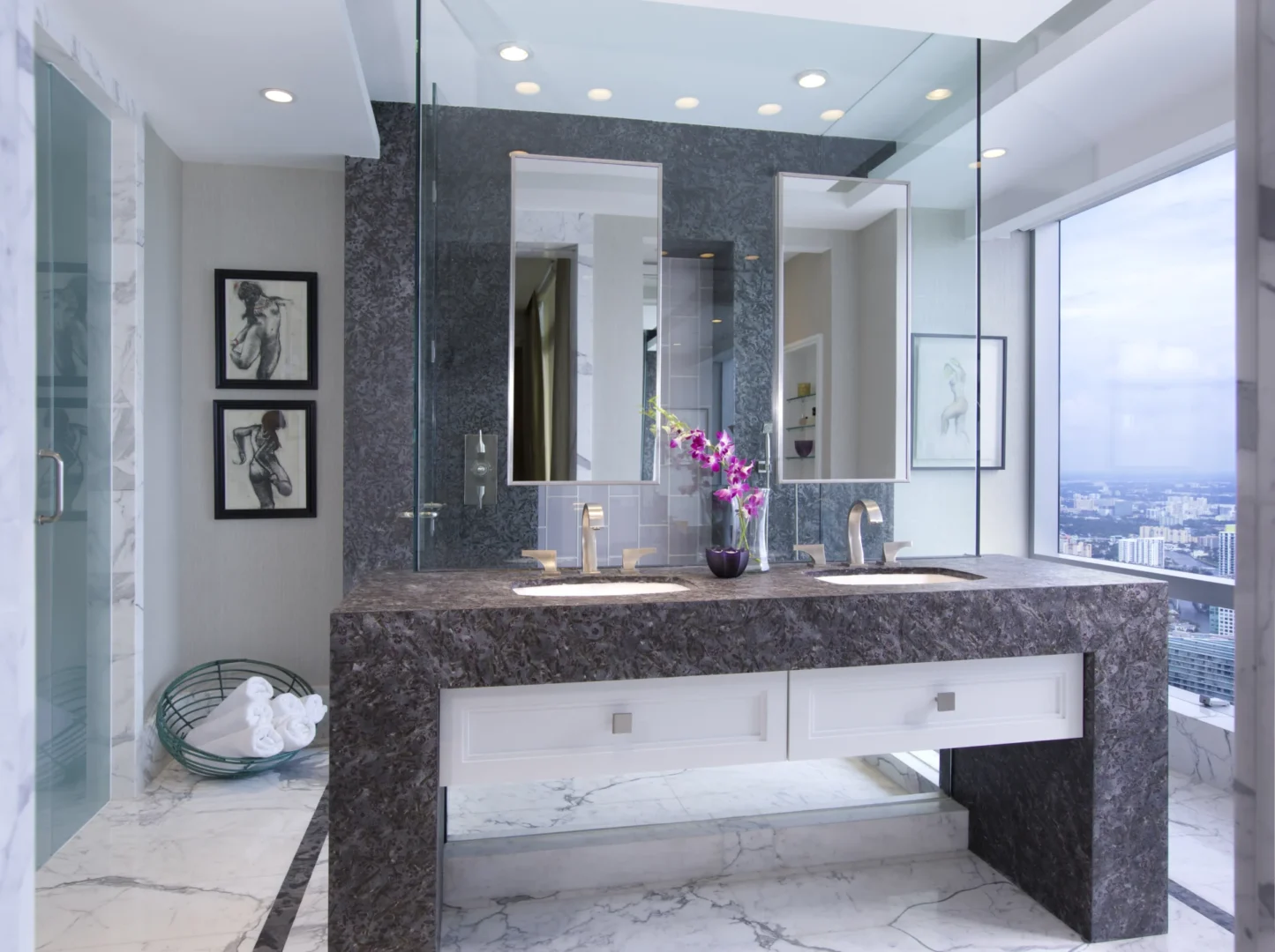 A dark stone double vanity with two sinks and white drawers sits in the Penthouse 4 bathroom overlooking a cityscape
