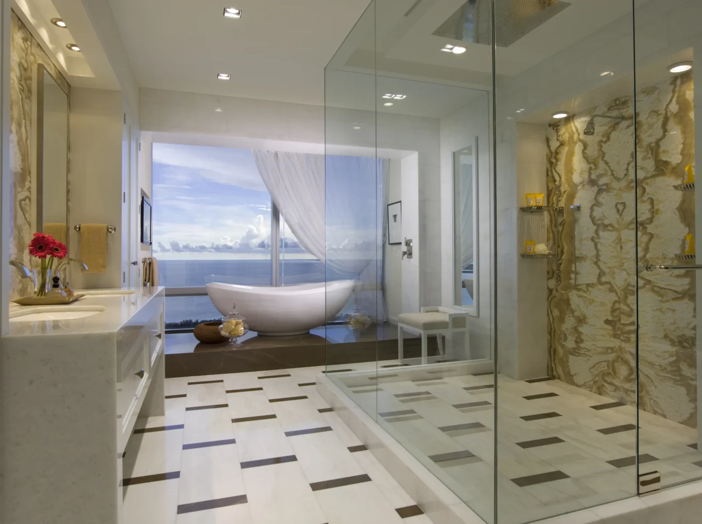 A white bathtub and glass shower enclosure are in the Penthouse 4 bathroom next to a window with an ocean view