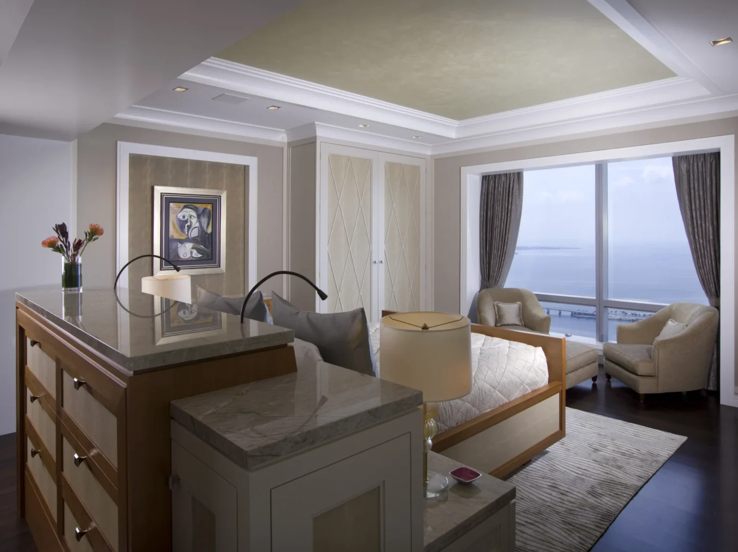 A bed and marble-topped cabinets are located in a Penthouse 4 bedroom with armchairs and large windows overlooking water