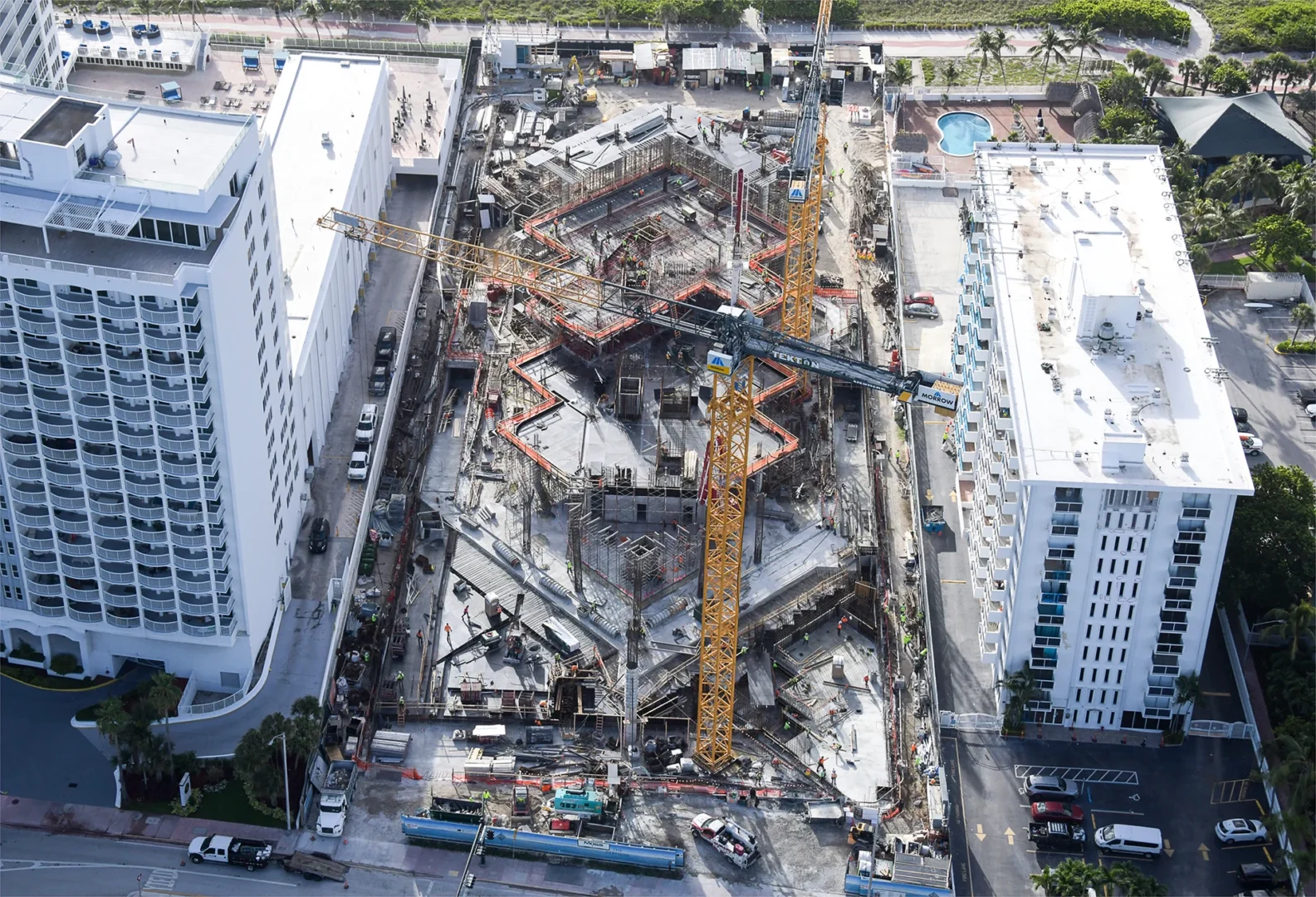 Yellow construction cranes stand over the structural framework of The Perigon between two white high-rise buildings