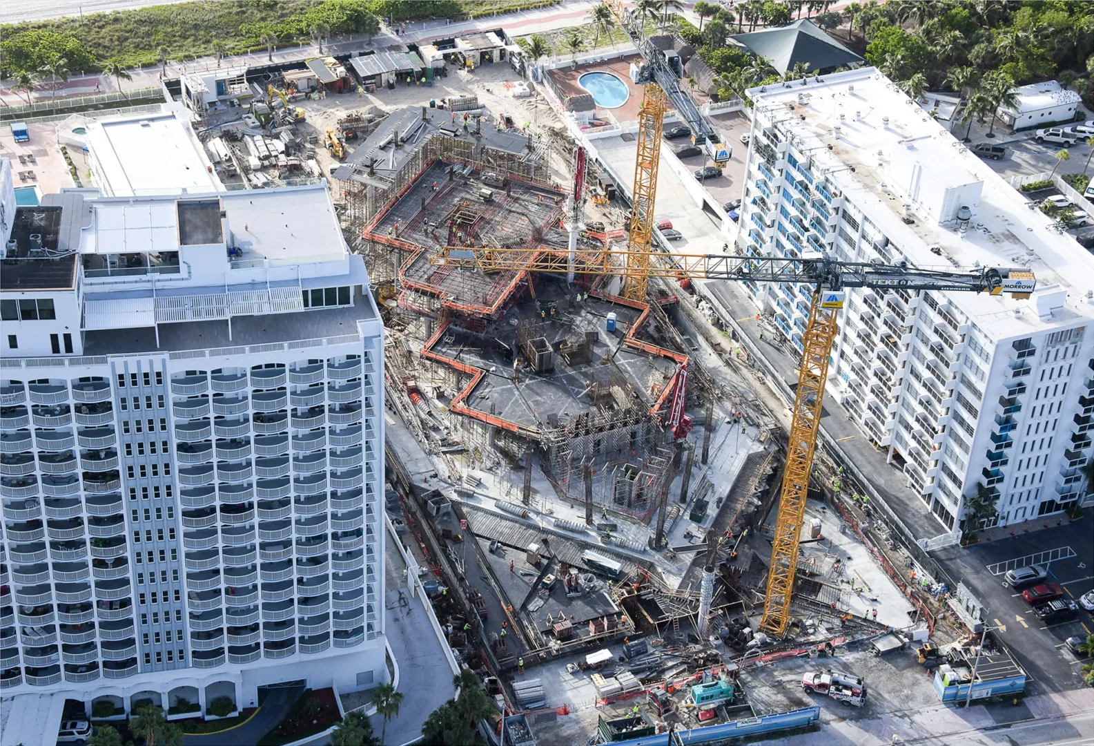 Two large yellow cranes stand above the construction site for The Perigon between white multi-story buildings