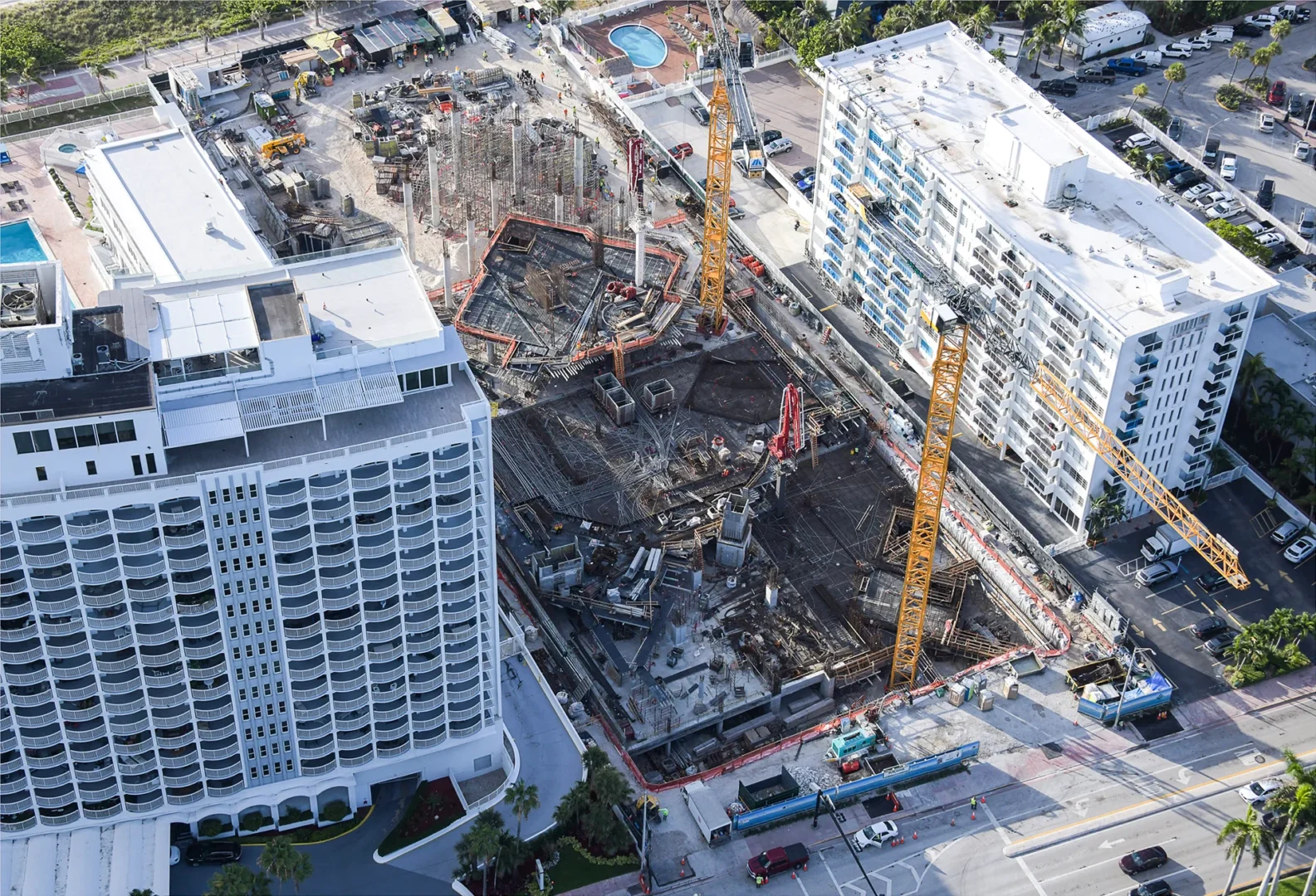 Yellow cranes stand over an active construction site for The Perigon between white multi-story buildings and adjacent streets