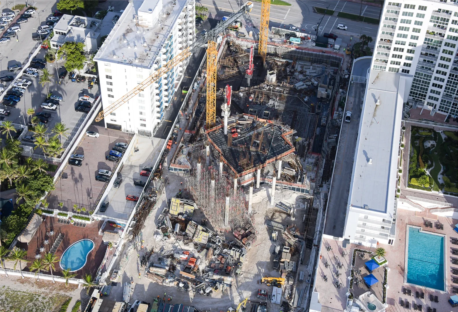 Cranes and scaffolding for The Perigon construction site are surrounded by urban buildings, streets, and a parking lot