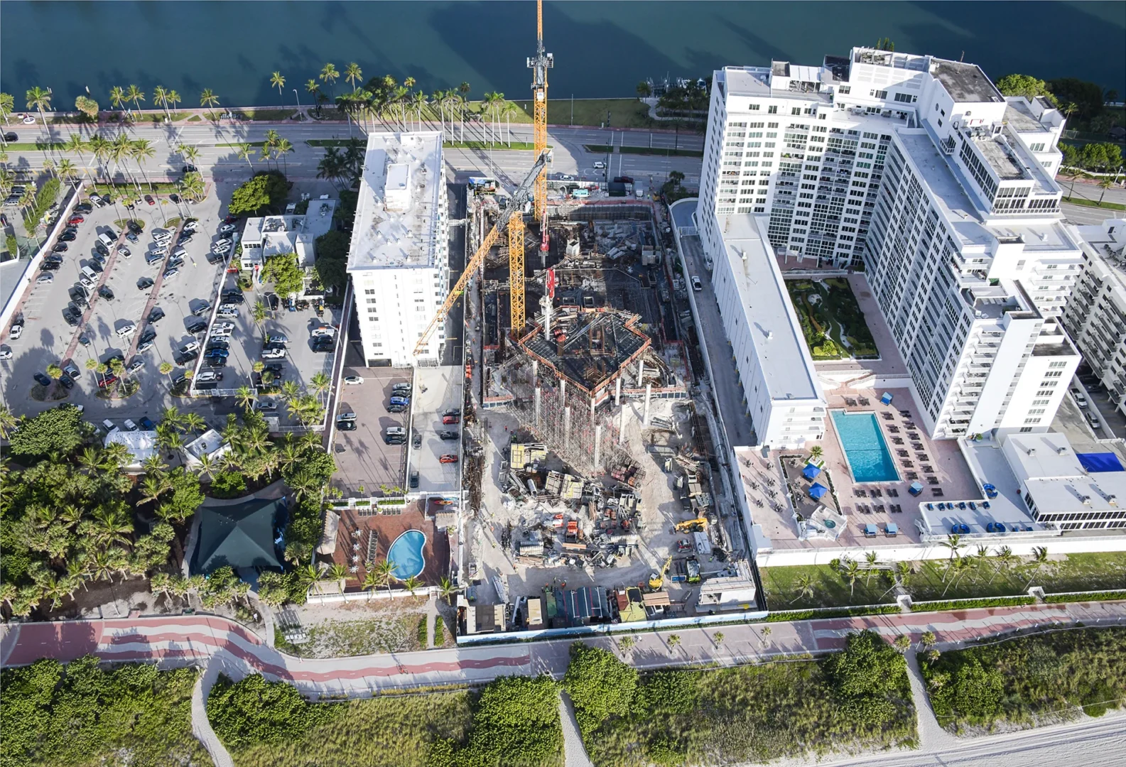 Construction cranes and a building site for The Perigon sit between white high-rise buildings, a parking lot, and water