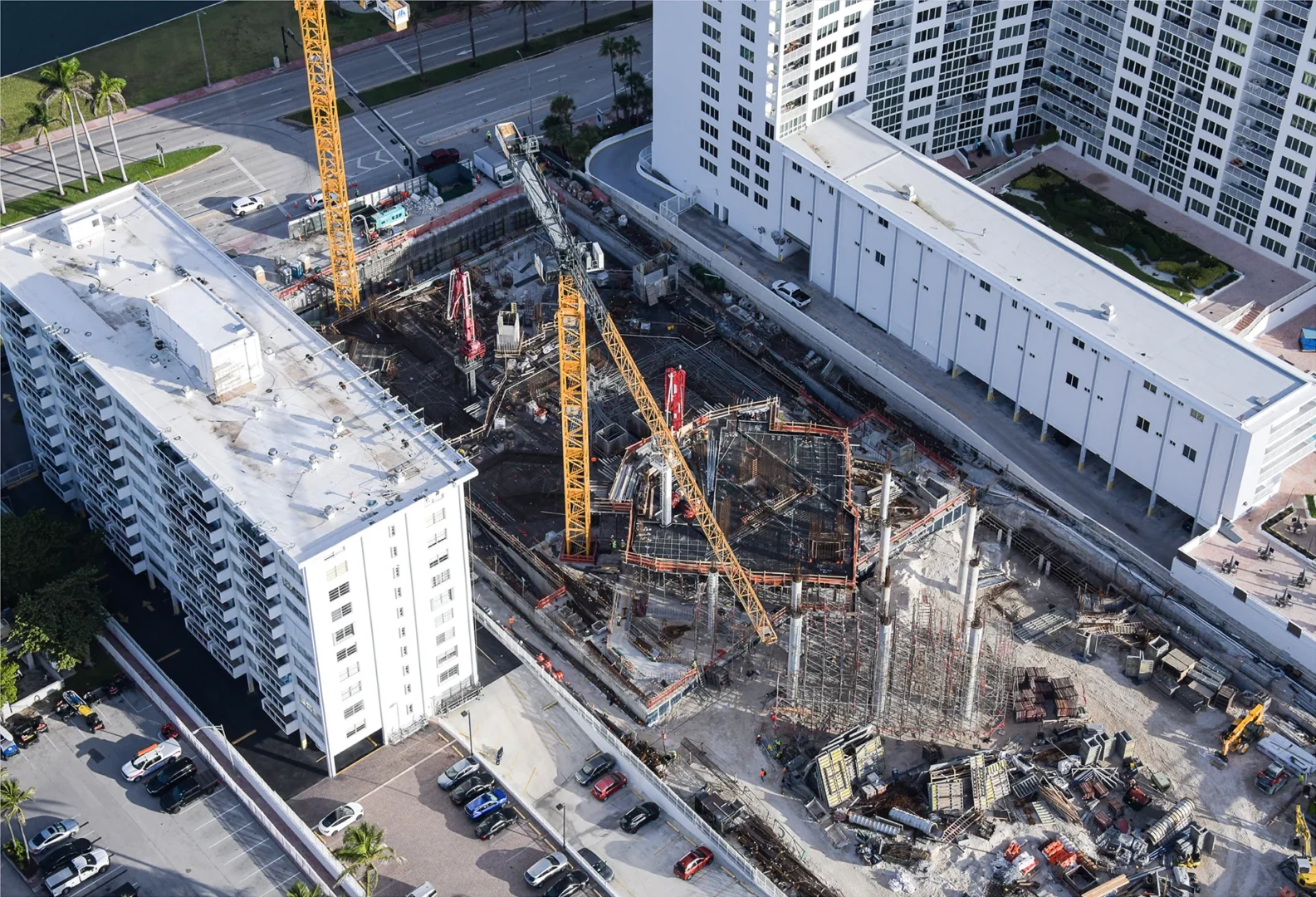 Yellow construction cranes stand over the building site for The Perigon, surrounded by white apartment buildings and parked cars