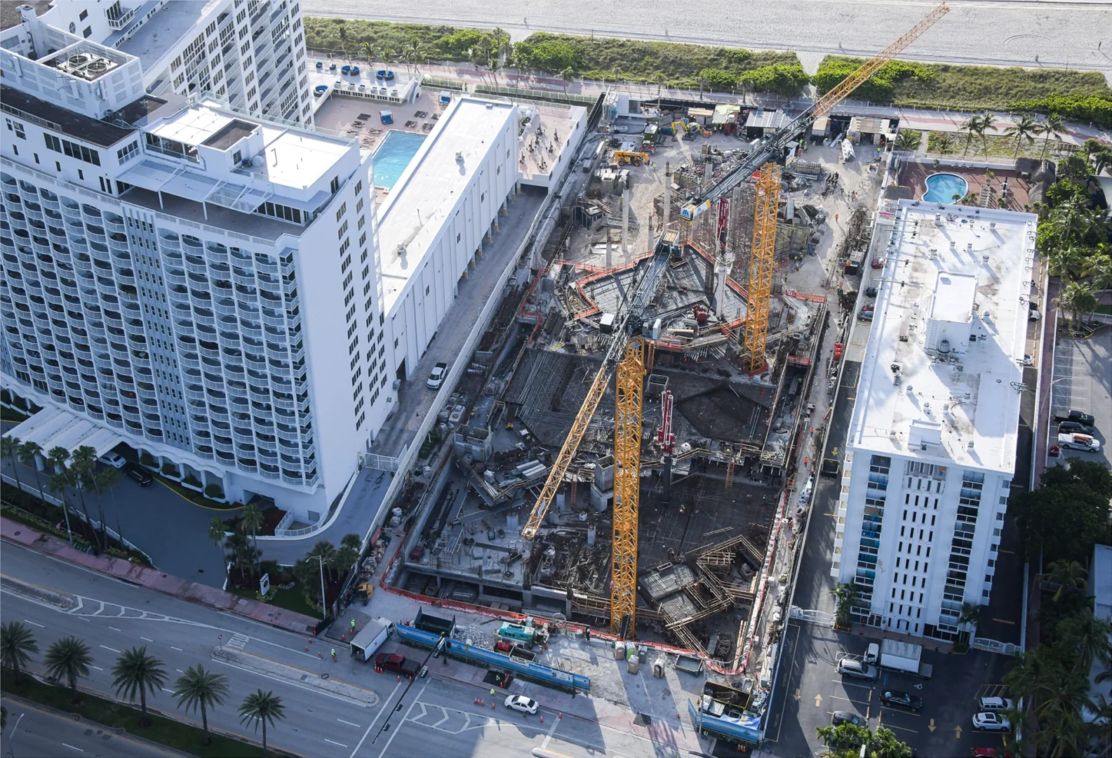 Yellow cranes and construction for The Perigon are located between white high-rise buildings near a street and beach
