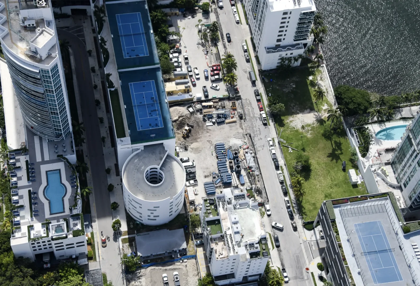 Blue tennis courts and high-rise buildings flank a street with vehicles at Villa Miami