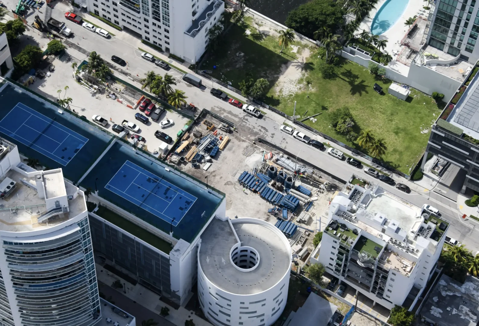 Blue tennis courts atop a building overlook a street with vehicles and construction equipment near Villa Miami