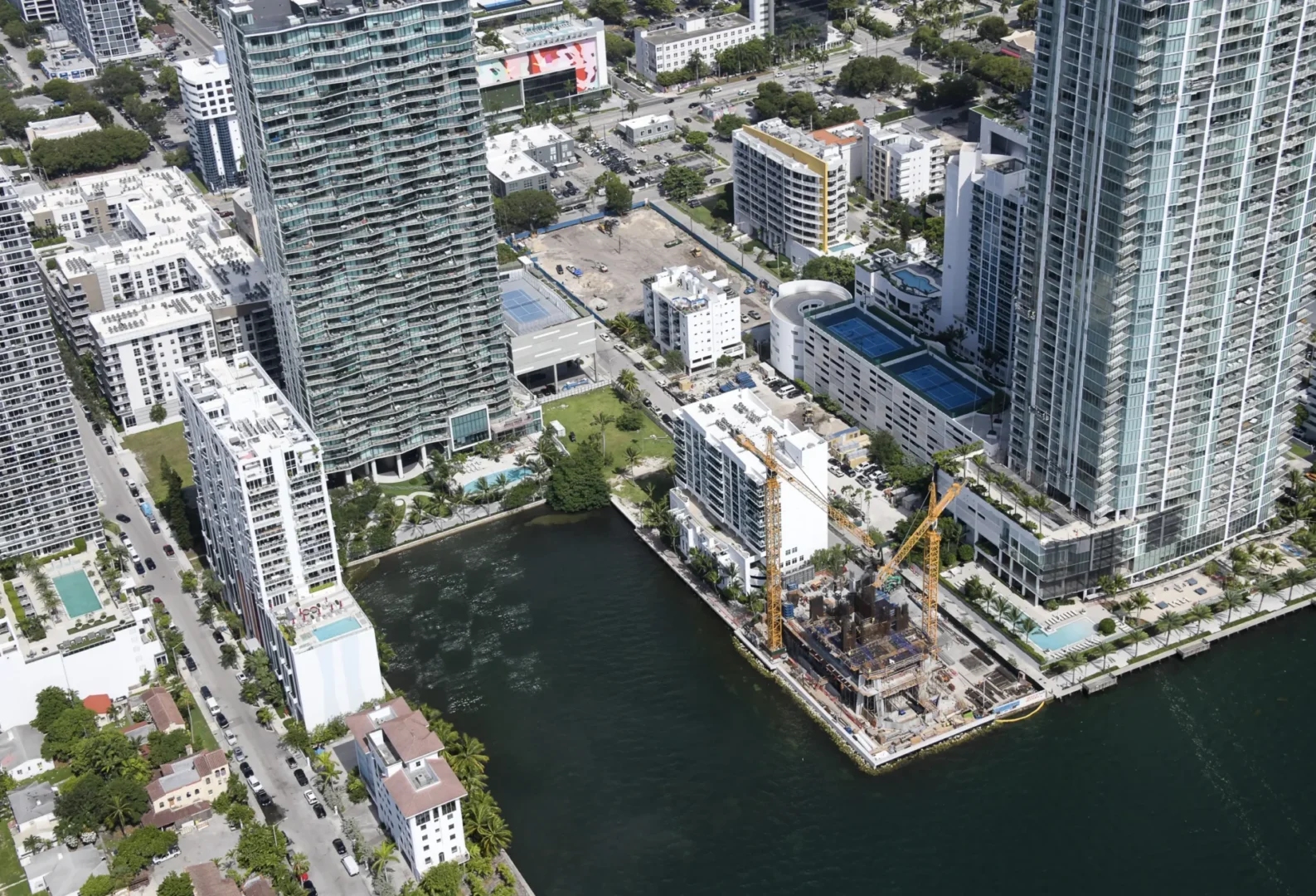 Skyscrapers and a waterfront construction site with cranes border a waterway near Villa Miami