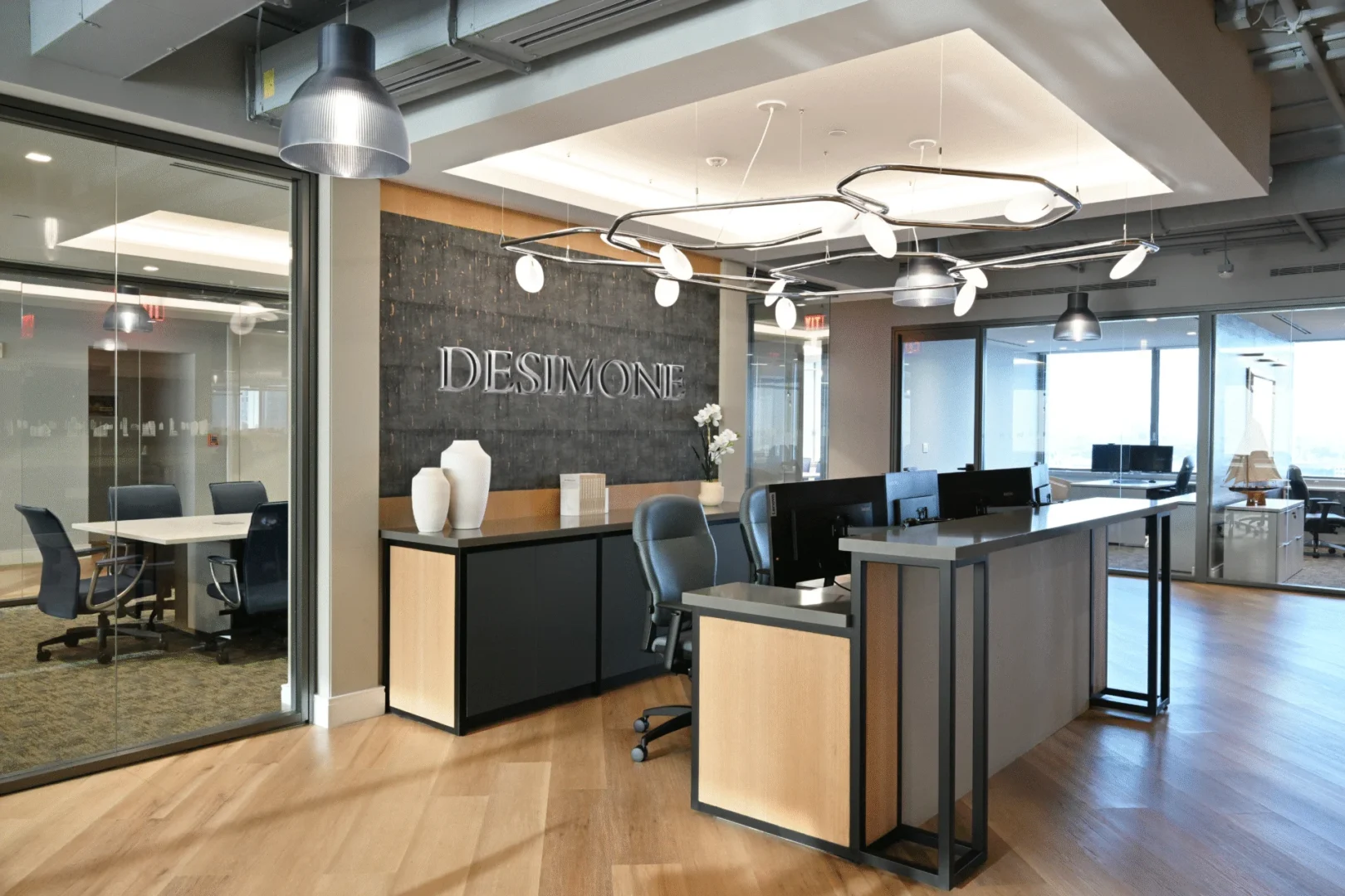 A reception desk in the DeSimone Office features a dark, textured wall with "DESIMONE" lettering under a modern light fixture