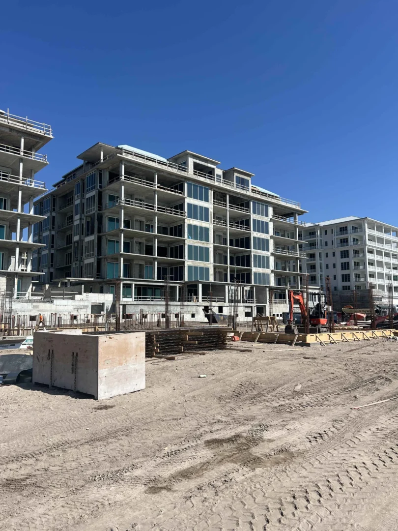 Un edificio de hormigón de varias plantas para el Four Seasons Resort & Residences de Naples Beach se alza sobre un terreno sin pavimentar, junto a una excavadora de color naranja.