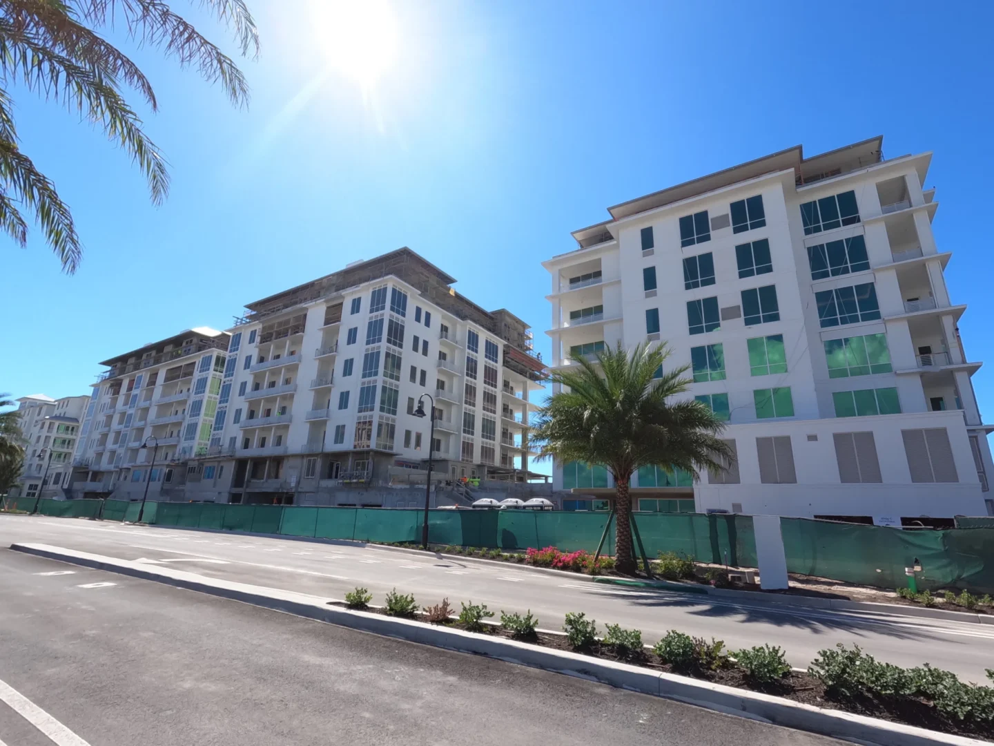 Los edificios blancos del Four Seasons Resort & Residences de Naples Beach se alzan tras una valla verde y palmeras, bajo un sol radiante.