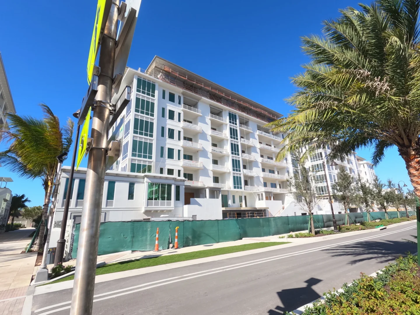 Un edificio blanco de varias plantas del Four Seasons Resort & Residences de Naples Beach se alza detrás de una valla verde y unas palmeras
