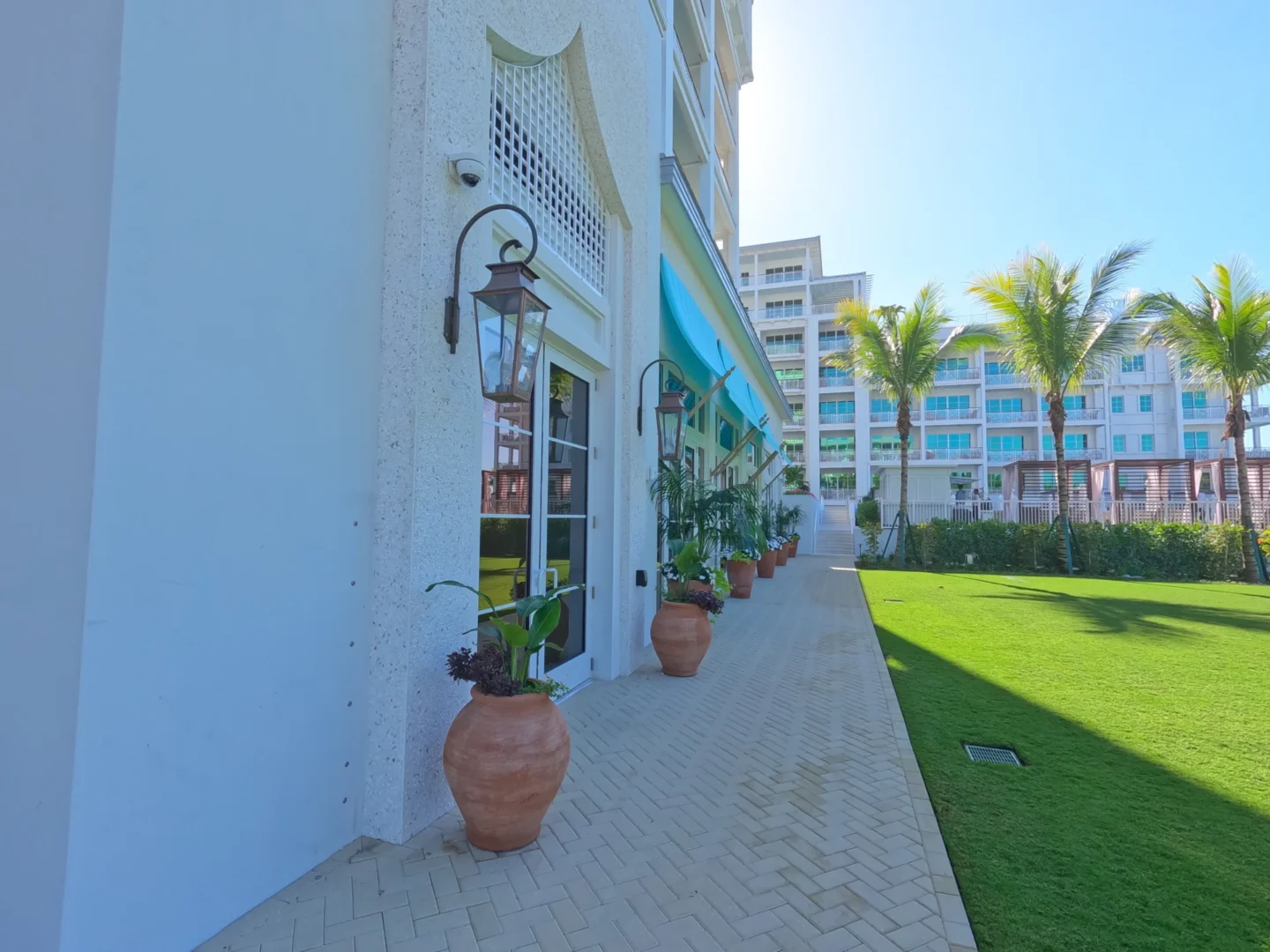 Un edificio blanco con plantas en macetas y una lámpara bordea una terraza pavimentada y un césped en el Four Seasons Resort & Residences de Naples Beach.