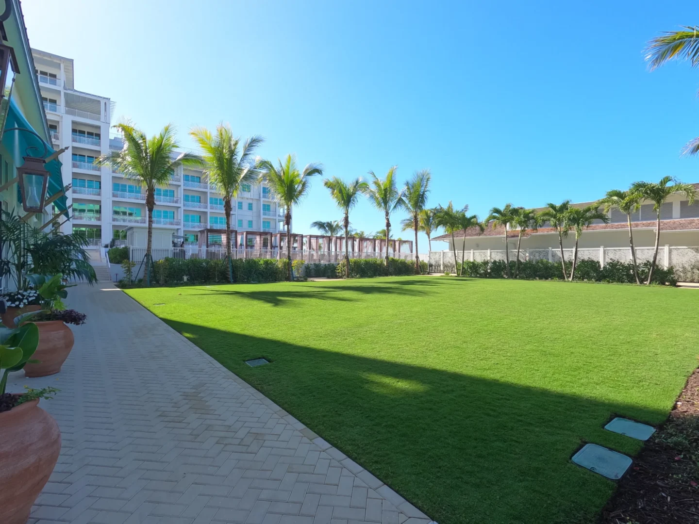 Un césped verde y un camino pavimentado bordean las palmeras y los edificios del Four Seasons Resort & Residences de Naples Beach.
