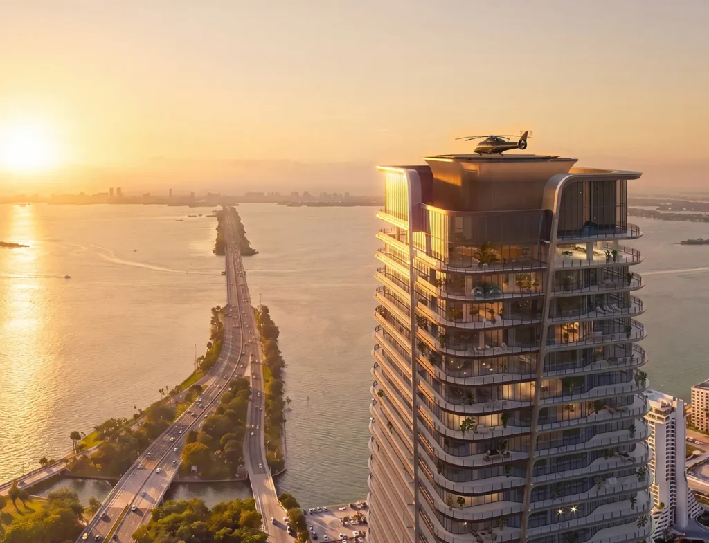 A tall skyscraper with terraces and a rooftop helicopter stands beside a long highway bridge crossing water during sunset