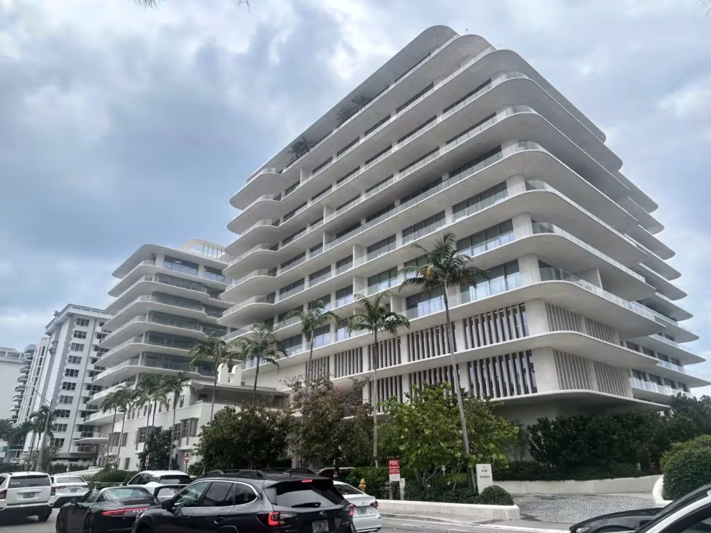 Un gran edificio blanco de Hillcrest, con balcones curvos, se alza detrás de las palmeras y los coches bajo un cielo nublado