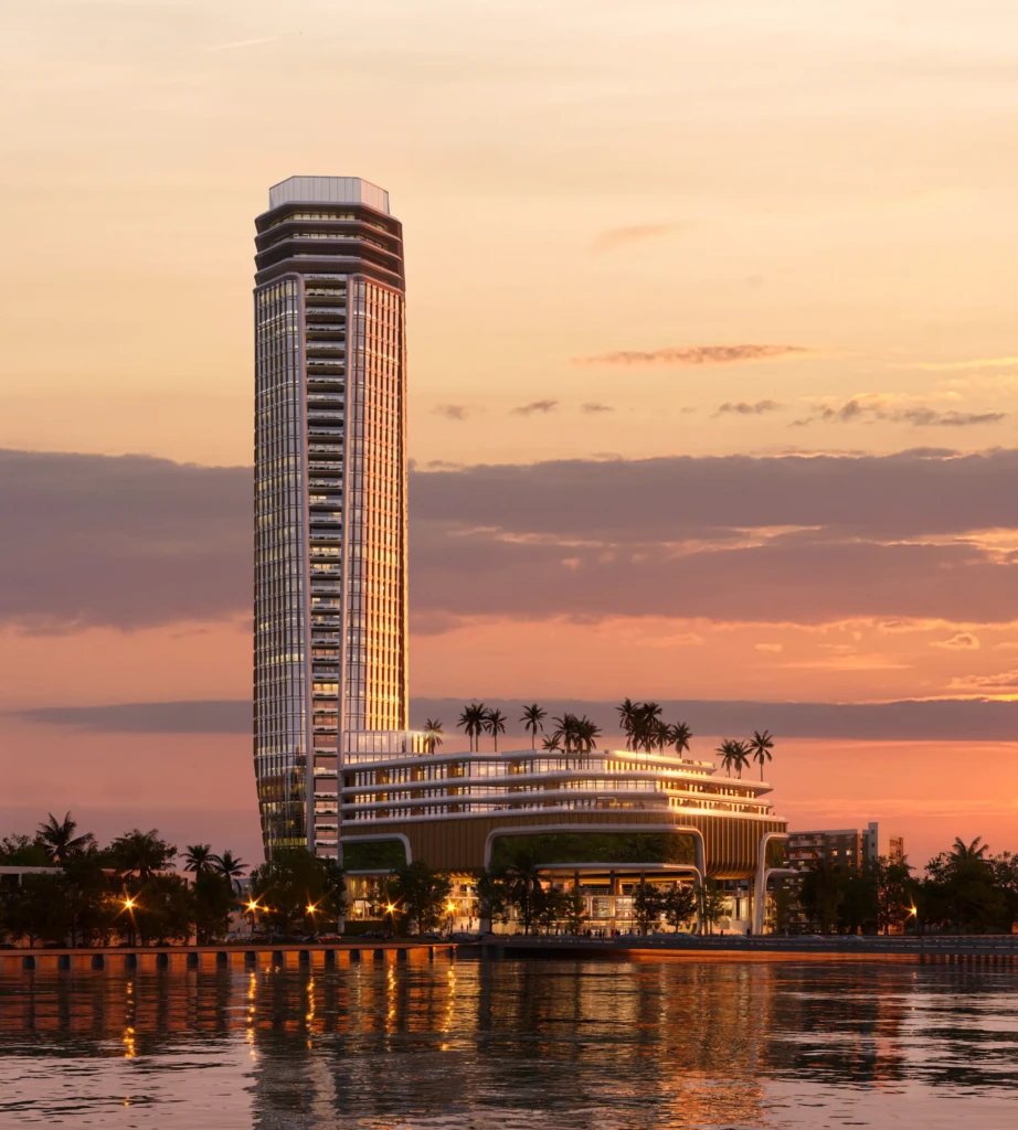 Una alta torre y un edificio curvo de «Isles Of Dreams» se alzan junto al agua bajo un cielo vespertino